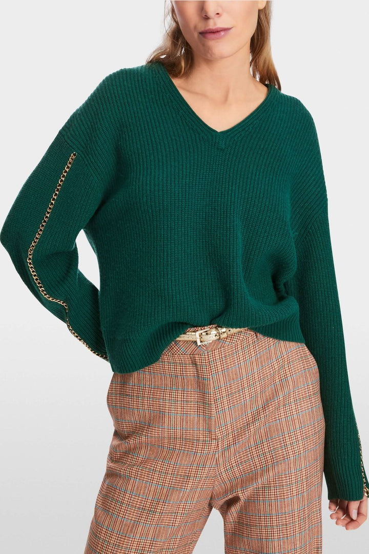 Pull en mailles vert avec col en V et chaîne sur la manche, coupe large et décontractée, style tendance.
