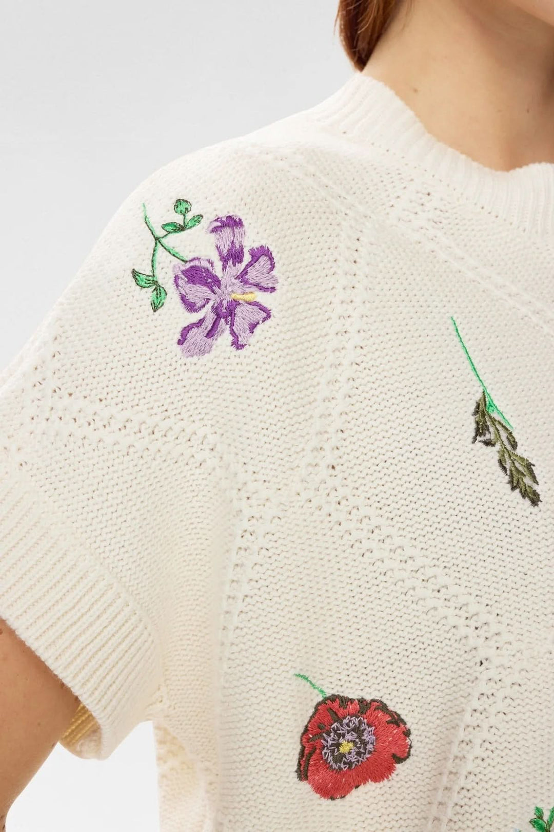 Chandail en tricot brodé à manches courtes avec motifs floraux colorés et court texturé, col rond classique et finition côtelée.