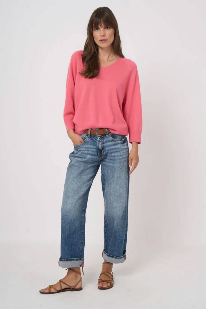 Femme portant un chandail en tricot à col en V rose avec jean décontracté, mettant en valeur un look moderne et intemporel.