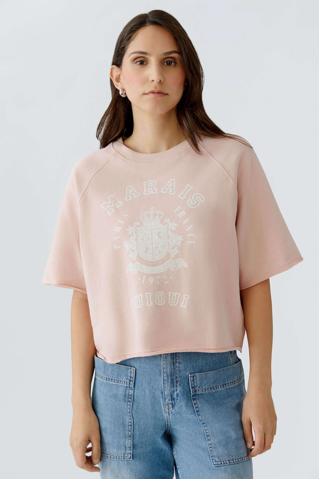 Femme portant un chandail imprimé graphique rétro, coupe ample et manches courtes, style décontracté et moderne.