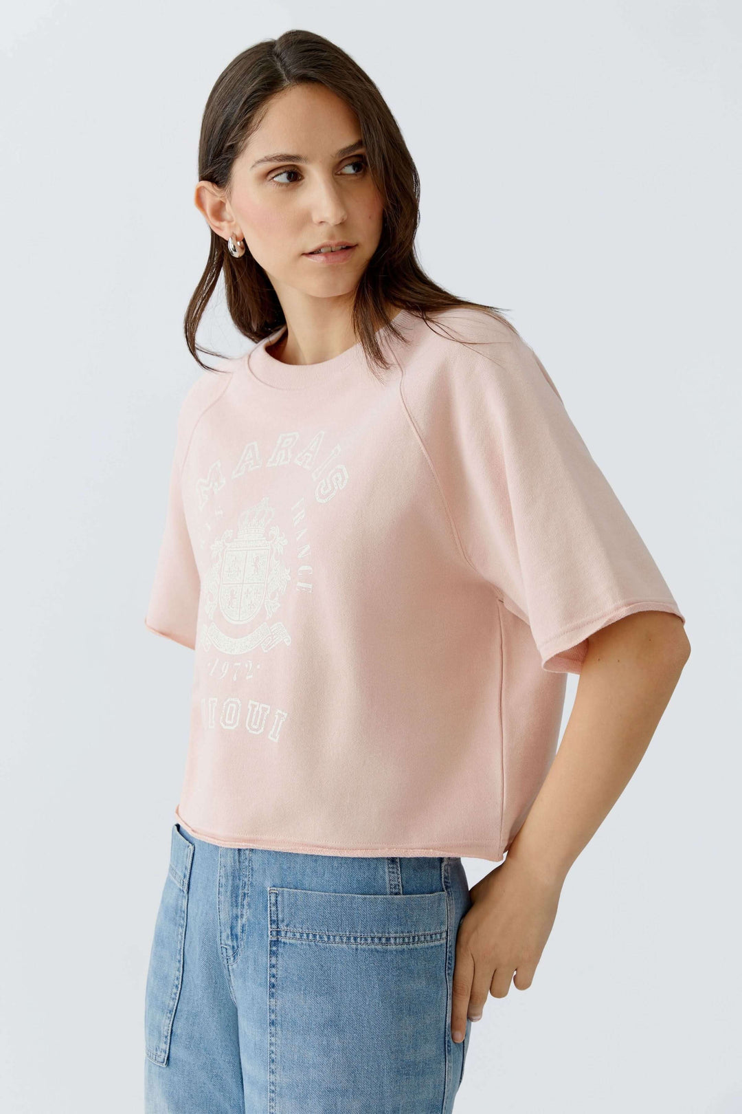 Femme portant un chandail imprimé graphique à manches courtes, coupe ample et raccourcie, idéal pour un look casual et moderne.