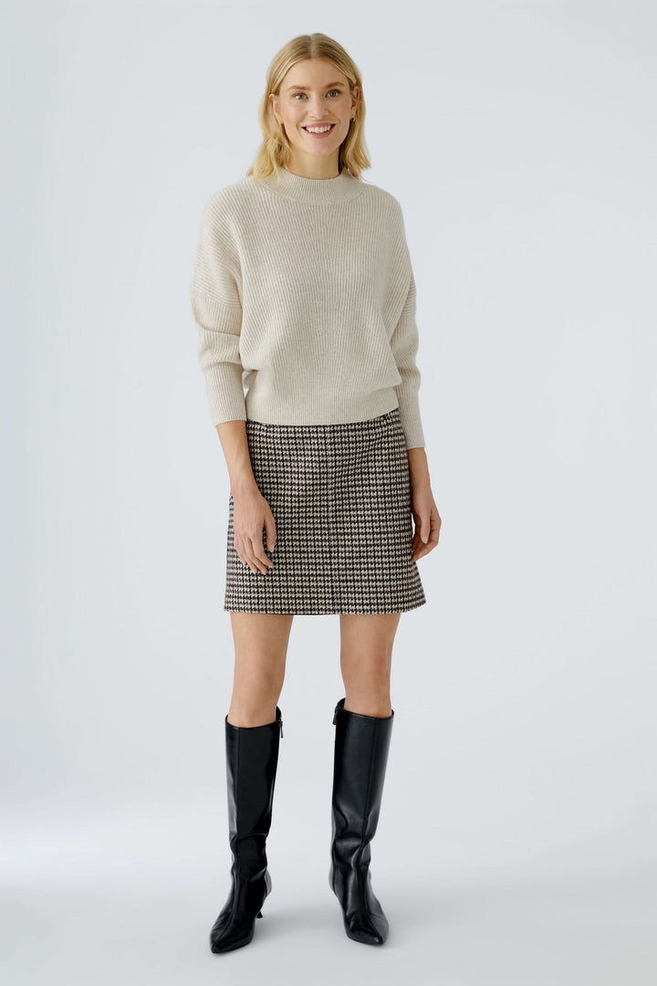 Chandail en maille fine à col montant, jupe à motifs, et cuissardes pour un look chic et moderne.