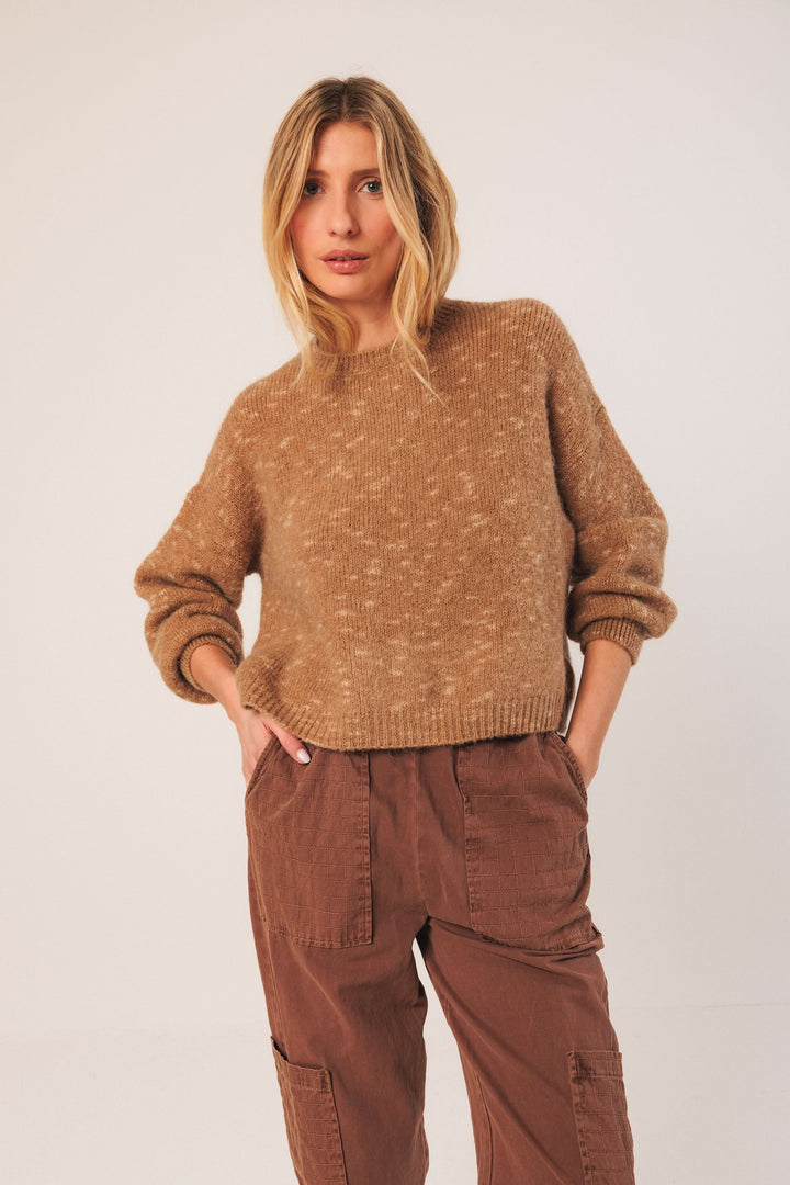 Chandail maille texturée beige à col rond et manches bouffantes, porté avec un pantalon marron, style décontracté.