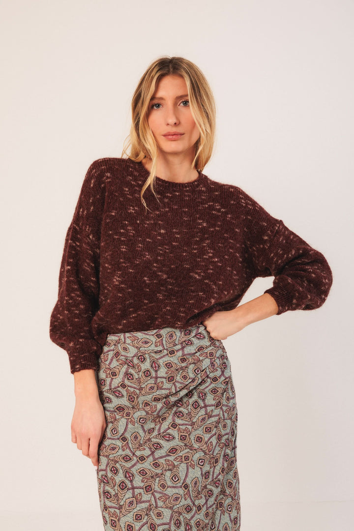 Chandail maille texturée bordeaux avec manches bouffantes, porté avec une jupe imprimée pour un look tendance.