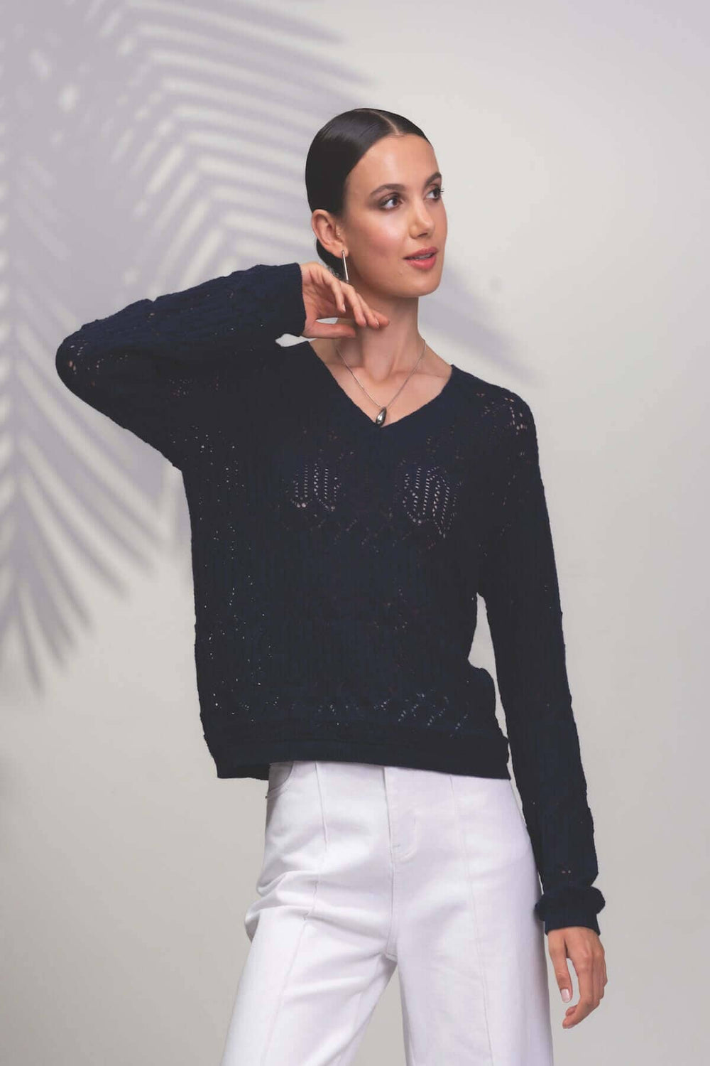Chandail à motifs géométriques avec encolure en V, créant un look élégant et original, porté avec un pantalon blanc.