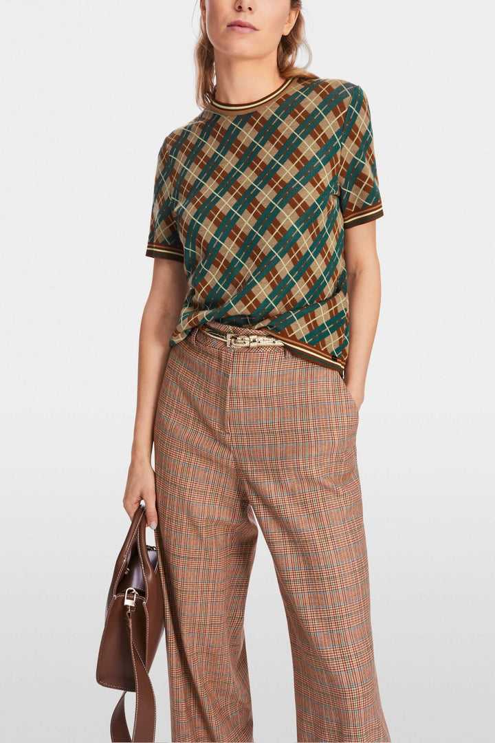 Chandail à motifs losanges avec bords côtelés, manches courtes et coupe ample, porté avec un pantalon à carreaux.