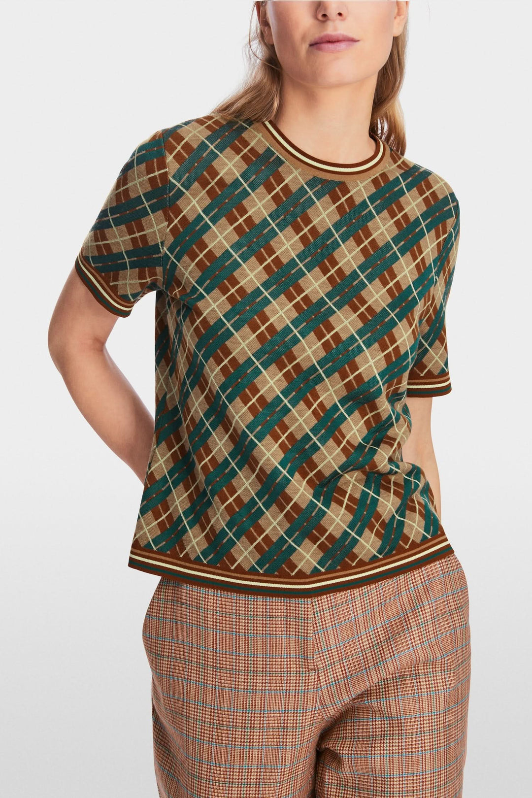 Chandail à motifs losanges en laine douce avec encolure ronde et manches courtes, porté avec un pantalon à carreaux.