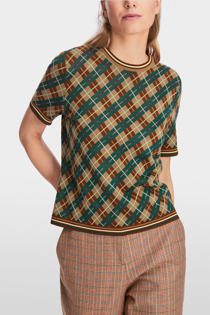 Chandail à motifs losanges en laine douce avec encolure ronde et manches courtes, porté avec un pantalon à carreaux.