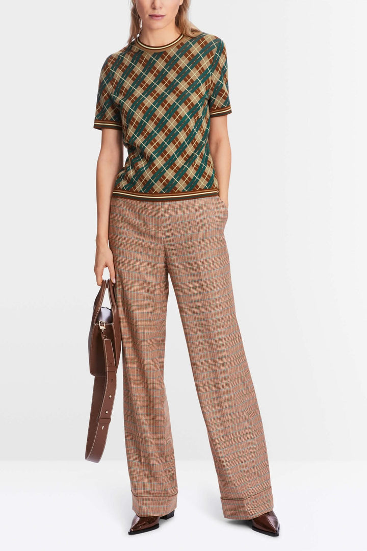 Chandail à motifs losanges avec bords côtelés, porté avec un pantalon à carreaux, style chic et décontracté.