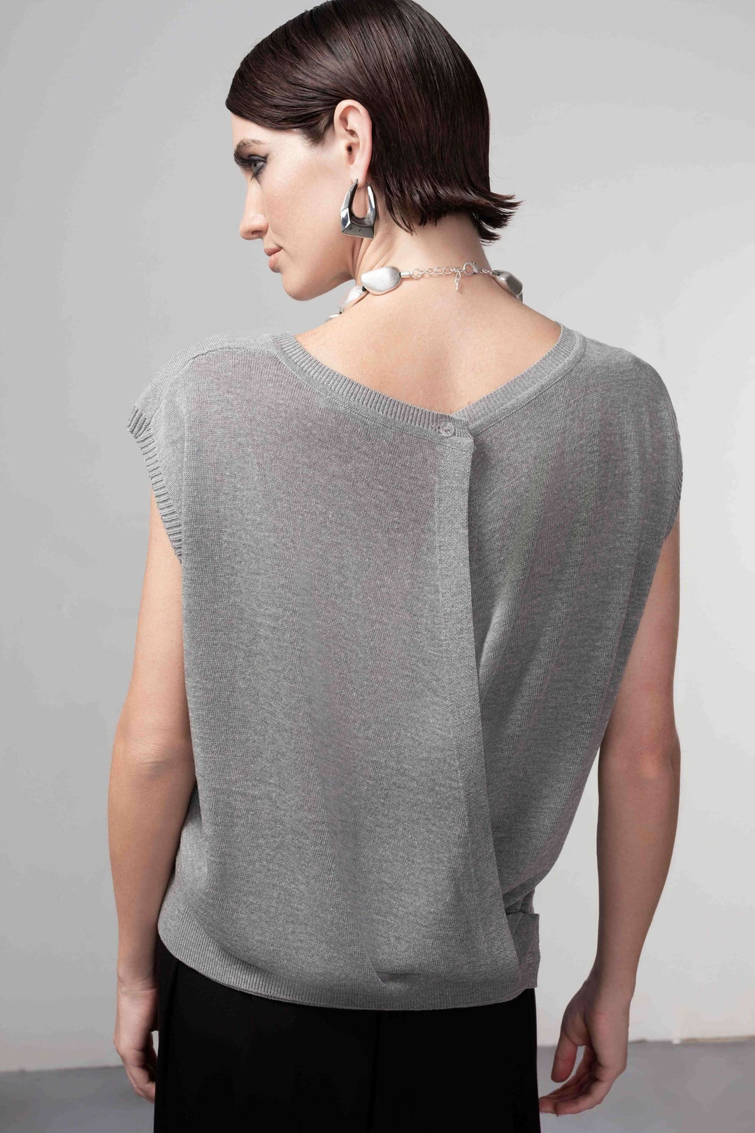 Femme portant un chandail sans manches avec ouverture au dos, coupe droite et maille fine. Chandail ouverture au dos chic et raffiné.