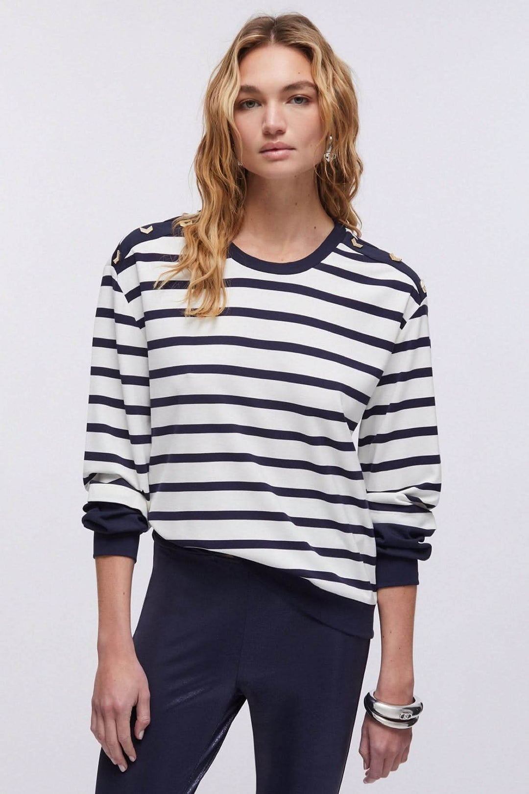 Femme portant un chandail rayé à manches longues avec détails décoratifs aux épaules, style décontracté et marin.