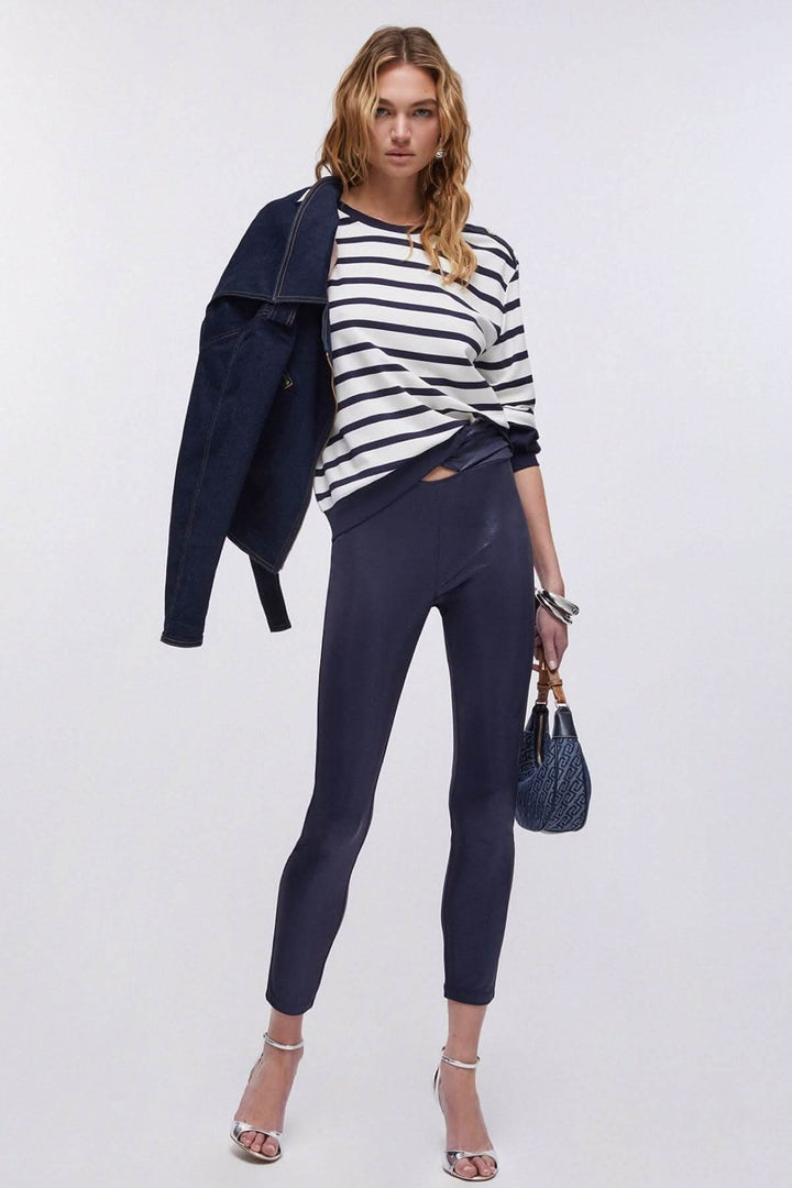 Femme portant un chandail rayé à manches longues avec une veste, un pantalon ajusté et des sandales argentées.