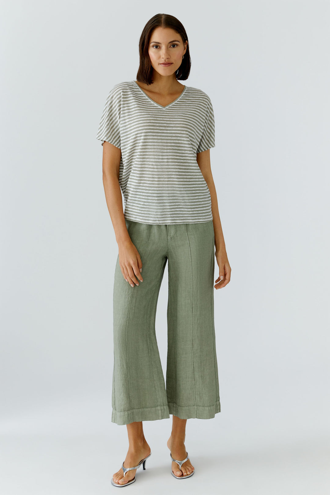 Femme portant un chandail à rayures col en v avec une coupe décontractée, manches courtes et un pantalon vert, style moderne et confortable.