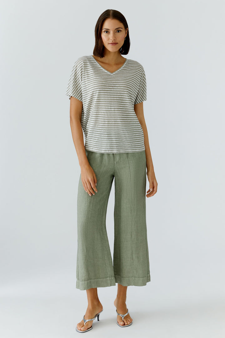 Femme portant un chandail à rayures col en v avec une coupe décontractée, manches courtes et un pantalon vert, style moderne et confortable.