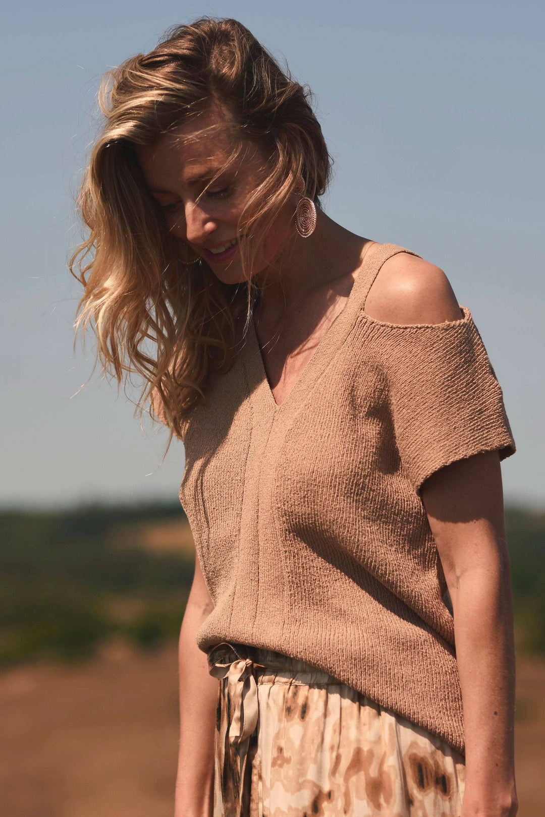 Chandail sans épaules beige à encolure en V, manches courtes, porté avec une jupe en pleine lumière.