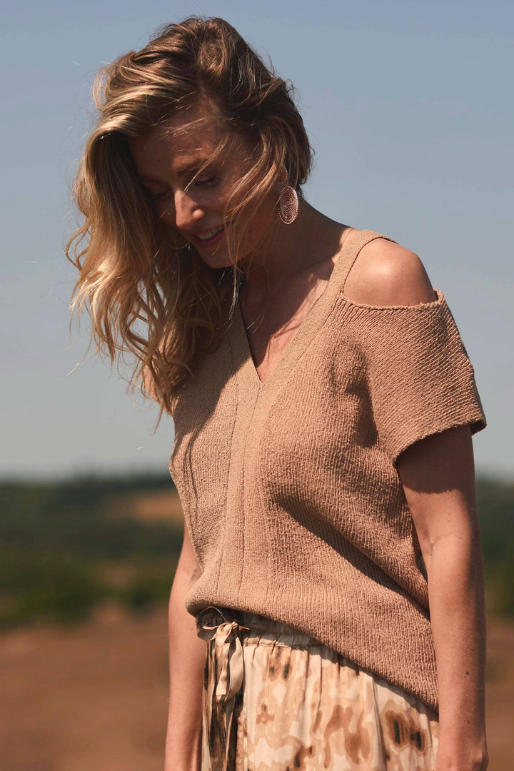 Chandail sans épaules beige à encolure en V, manches courtes, porté avec une jupe en pleine lumière.