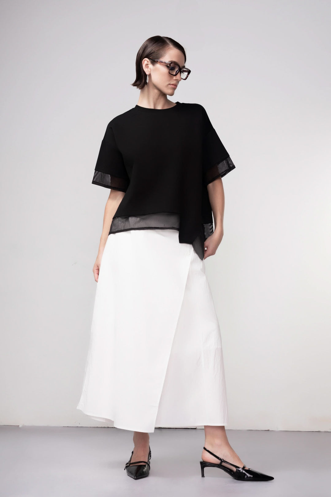 Femme portant un chandail texturé noir avec détails en maille ajourée, silhouette droite et ample, look contemporain et graphique.