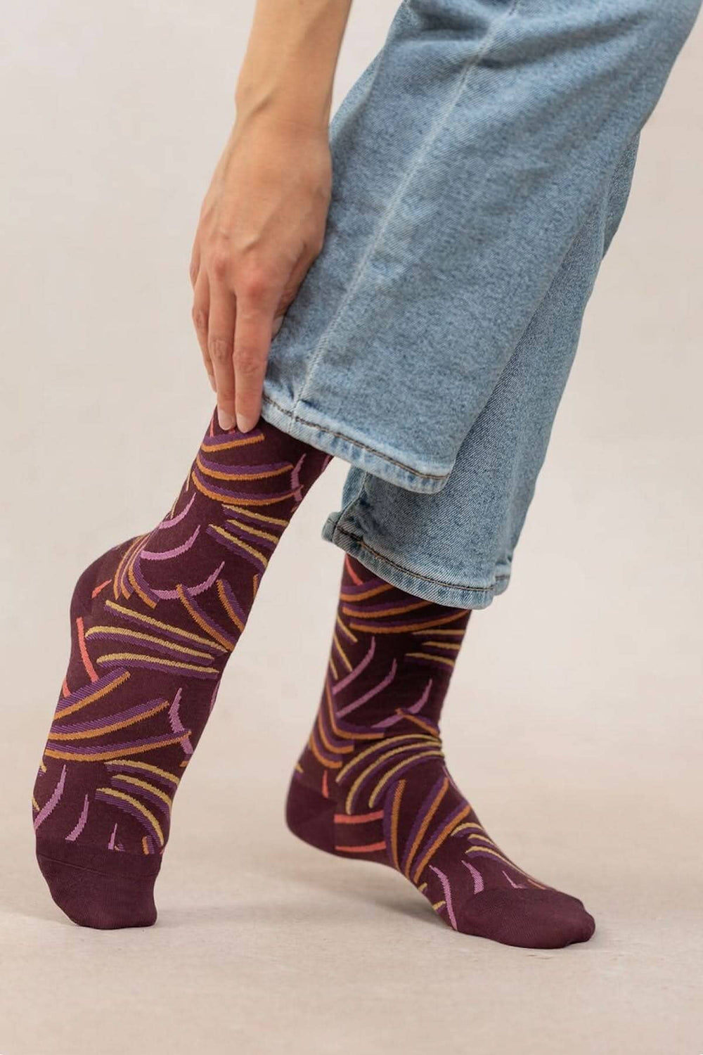 Chaussettes griffes en coton doux, motifs graphiques colorés sur fond bordeaux, portées avec un jean.
