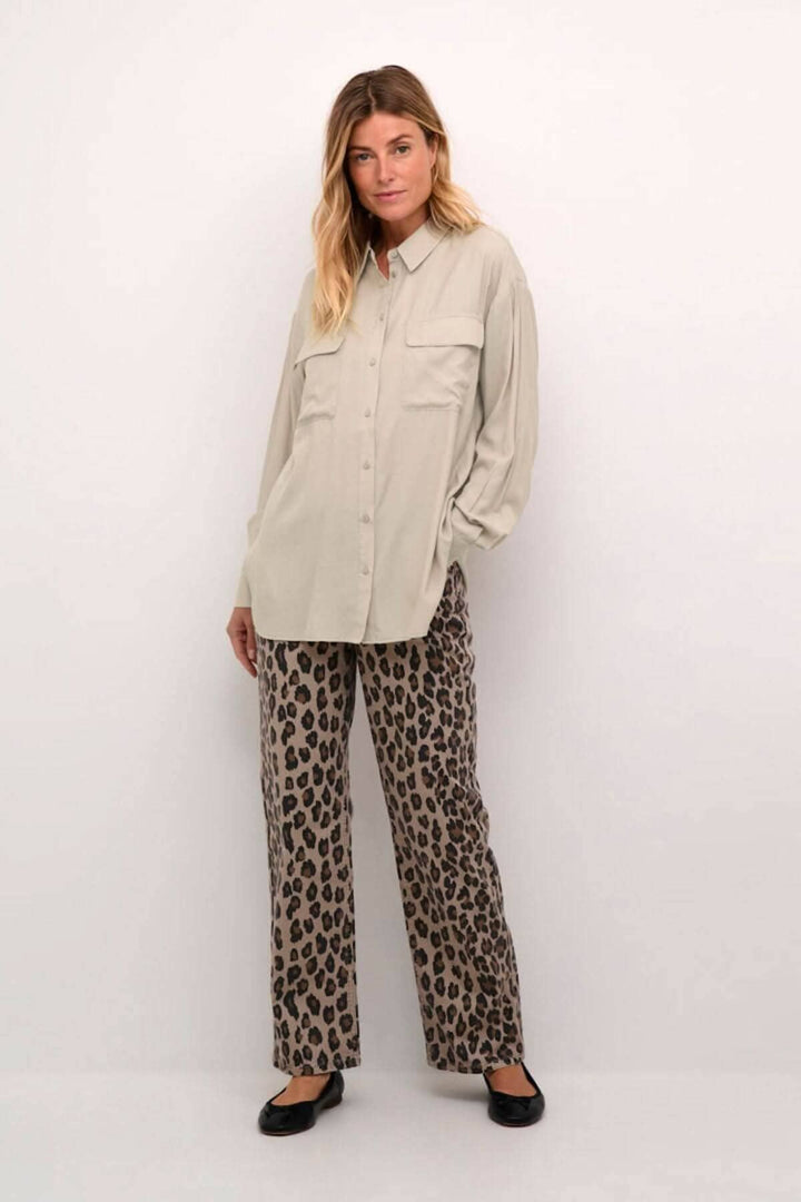 Chemise moderne beige avec poches, manches amples, pantalon léopard, look décontracté et soigné.