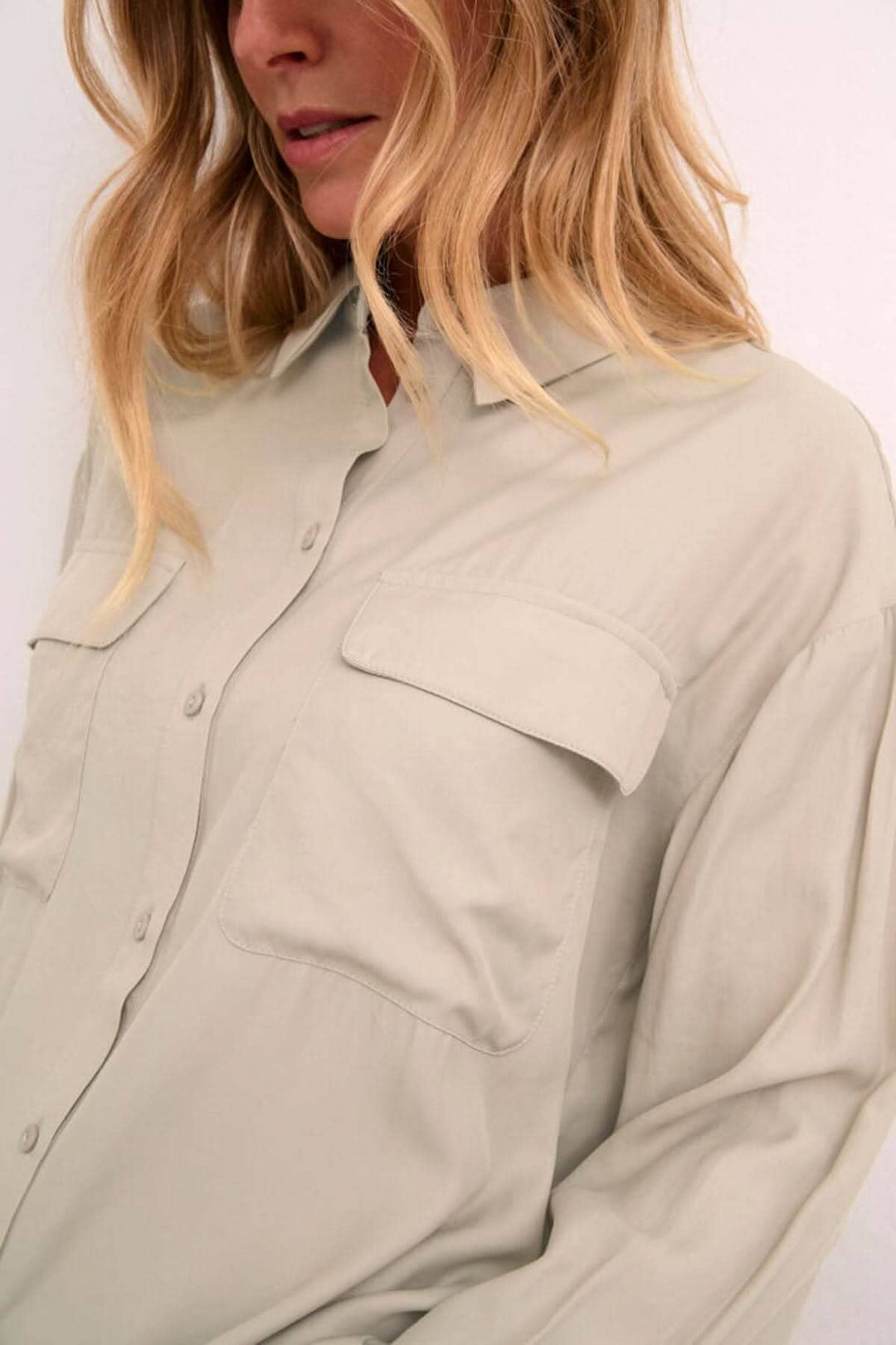 Chemise moderne beige avec poches plaquées, manches amples et col classique, style décontracté et soigné.