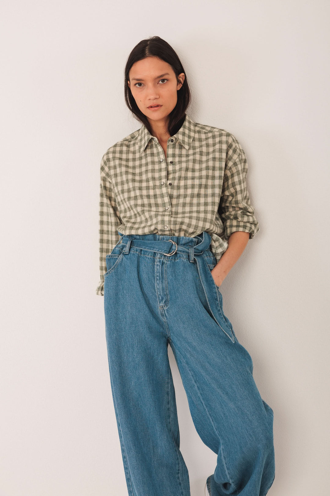 Chemise à carreaux verte avec manches retroussées, associée à un pantalon en denim large pour un look décontracté.