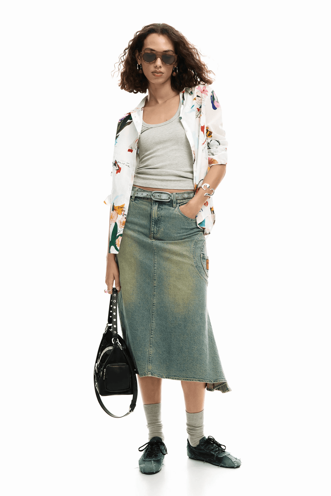 Femme portant une chemise collage fleurs avec une jupe en jean, lunettes de soleil et un sac noir, style élégant et décontracté.