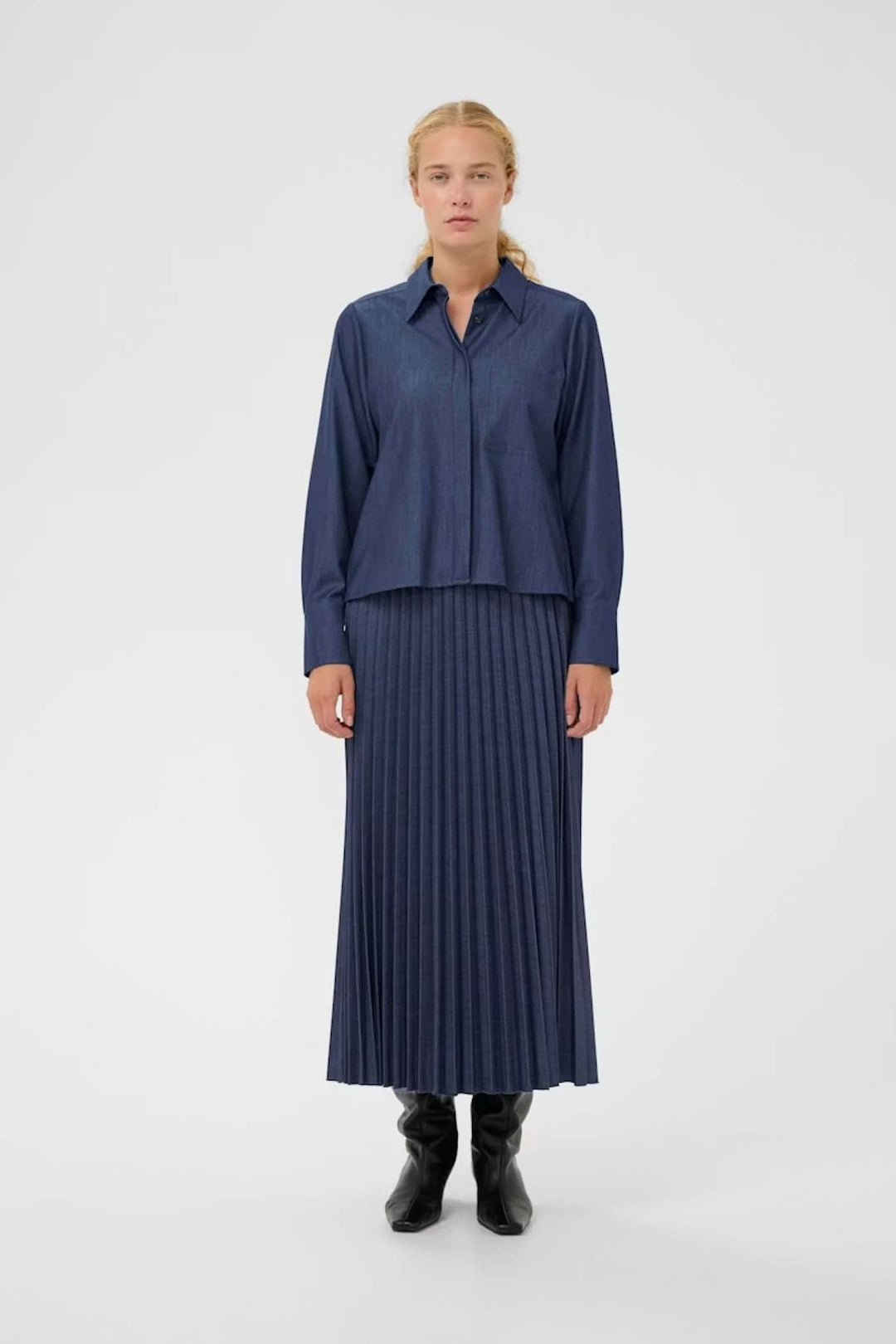 Chemise à coupe droite Cherrie élégante et polyvalente, portée avec une jupe plissée et des bottes pour un look moderne.