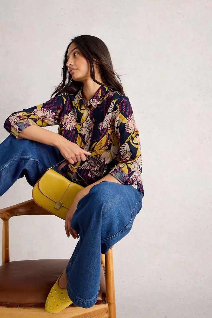 Femme portant une chemise florale colorée avec un sac jaune et des chaussures assorties, assise sur une chaise.