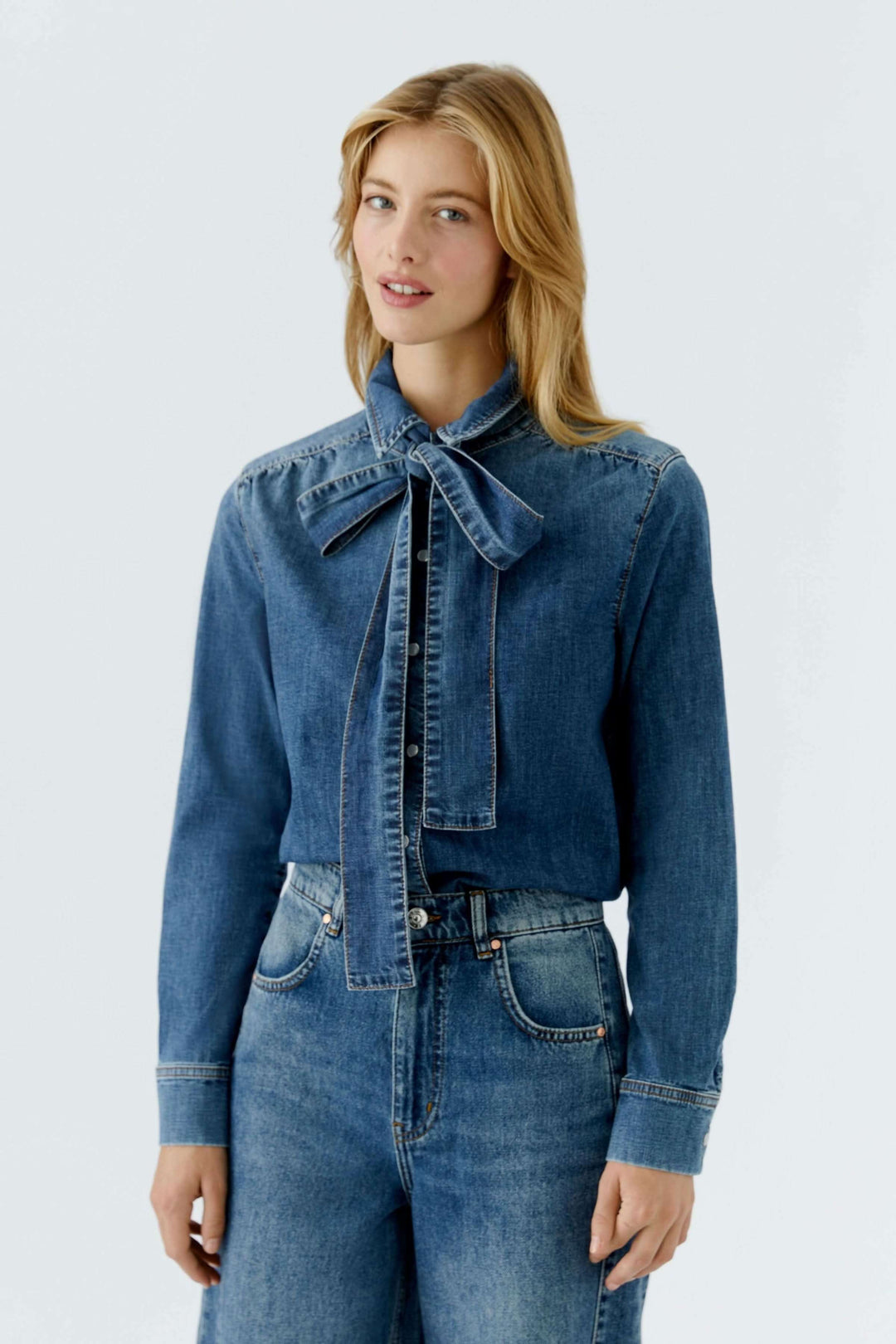 Femme portant une chemise en denim avec nœud amovible, montrant une élégance décontractée et moderne.