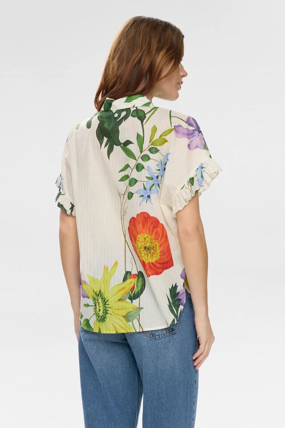 Dos de chemise fluide imprimée à manches volantées en tissu texturé avec motif floral vibrant, portée avec un jean décontracté.