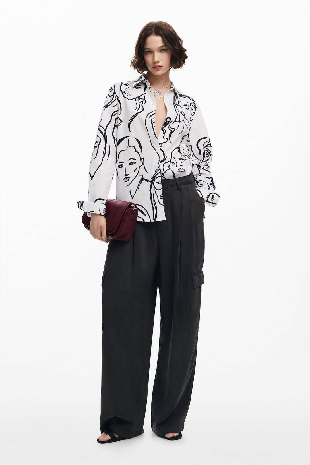 Chemise à imprimé visages artistiques portée avec un pantalon ample, ajoutant une touche chic et moderne.