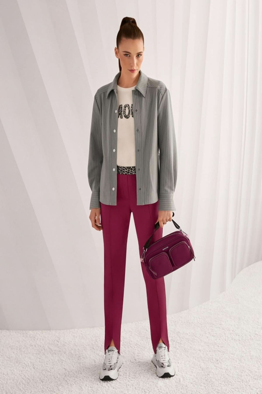 Femme portant une chemise rayée décontractée avec col classique, poignets, et boutons-pression, tenue avec pantalon rose et sac assorti.