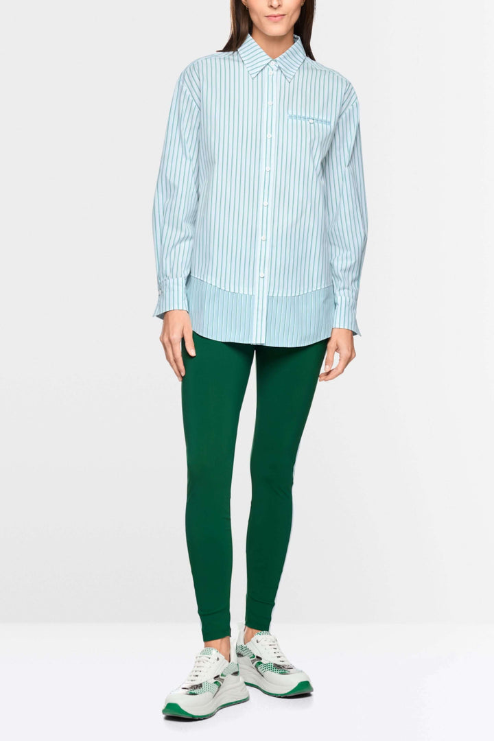 Chemise rayée en coton portée avec pantalon vert, affichant une silhouette moderne et allongée, idéale pour un look professionnel ou décontracté.