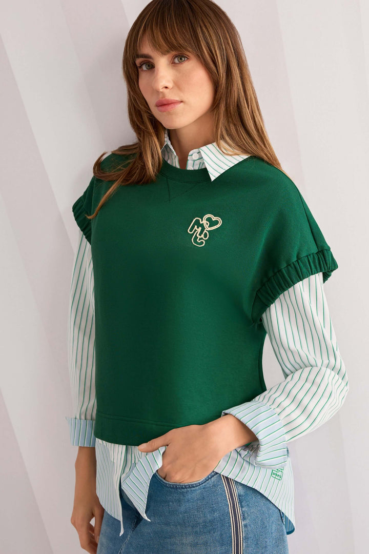Chemise rayée en coton portée avec un pull vert pour un look moderne et décontracté.