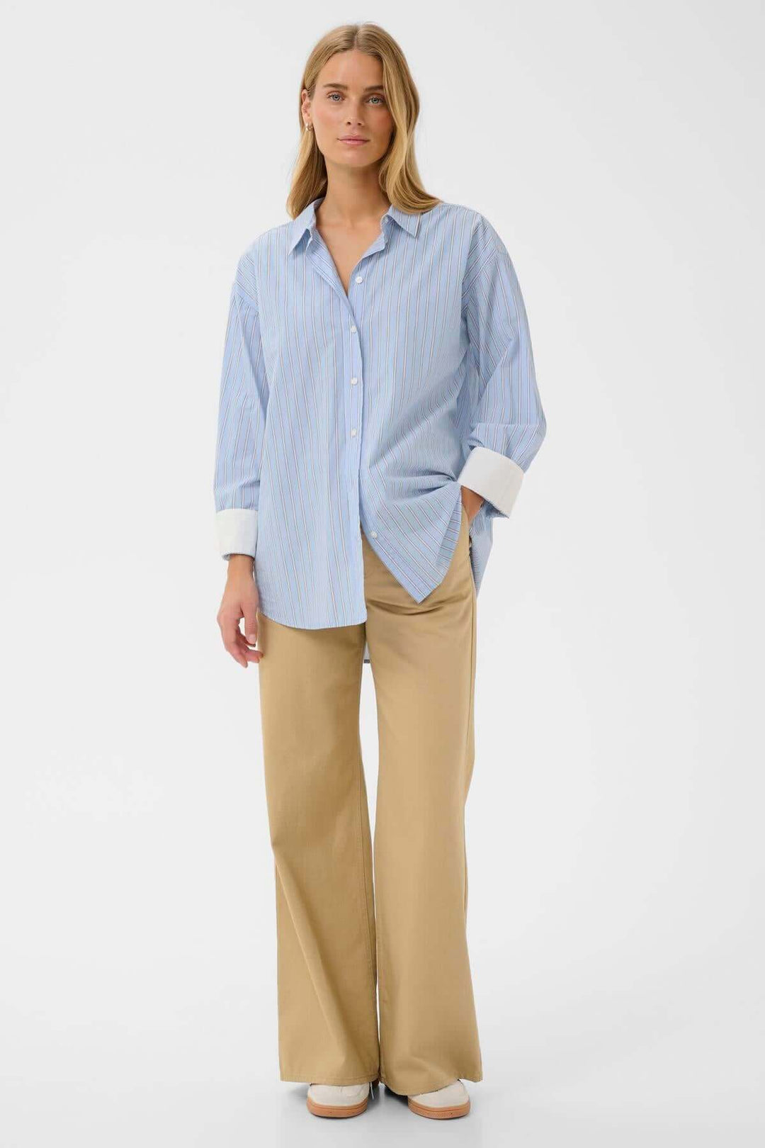 Femme portant une chemise à rayures fines Savanna bleu avec poignets contrastants, coupe droite et pantalon beige, look décontracté et moderne.