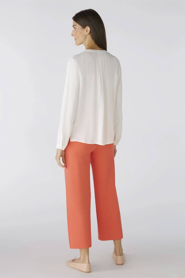 Femme portant une chemise blanche sans col et un pantalon corail, vue arrière, style décontracté.