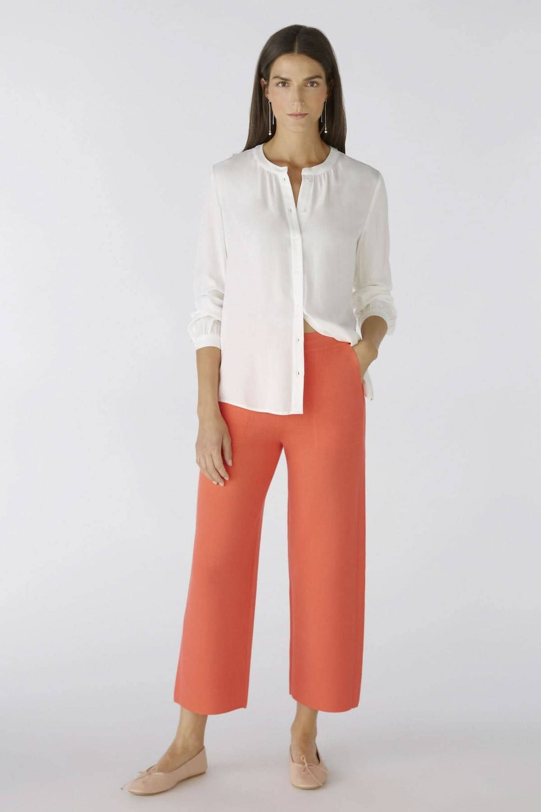 Modèle portant une chemise sans col blanche et un pantalon rouge, illustrant un style chic et décontracté.