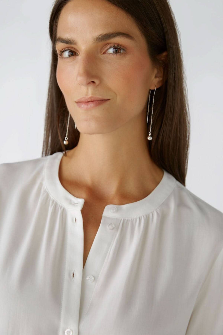 Chemise sans col blanche avec encolure ronde et détails de boutons, portée par un modèle avec de longues boucles d&