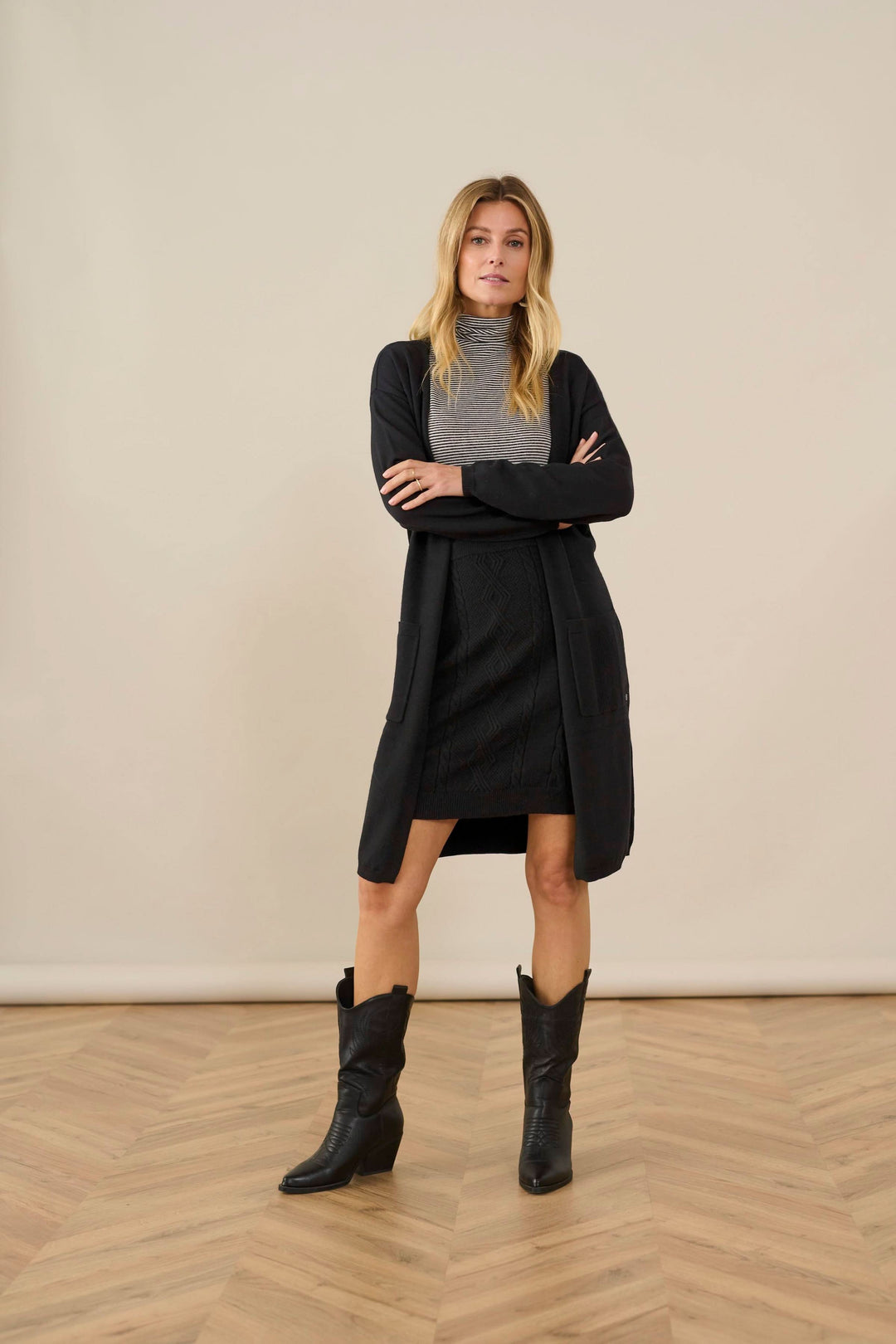 Modèle portant un col roulé Amma rayé gris et noir avec une jupe noire, bottes noires, sur fond neutre.
