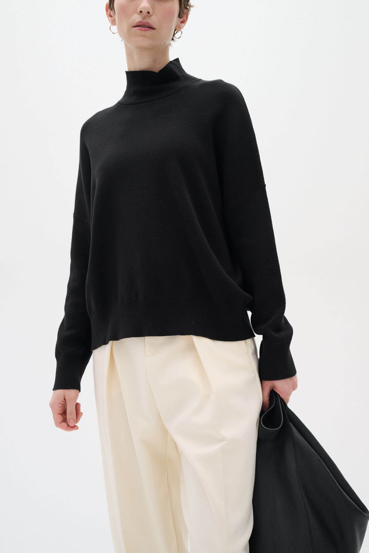 Chandail noir à col roulé Tenley, manches longues, porté avec un pantalon beige, stylé et décontracté.