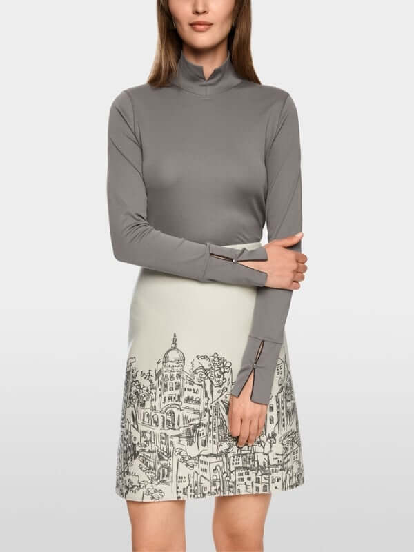 Femme portant un col roulé ajusté avec col fendu et fermetures zippées, associé à une jupe imprimée et une ceinture large élégante.