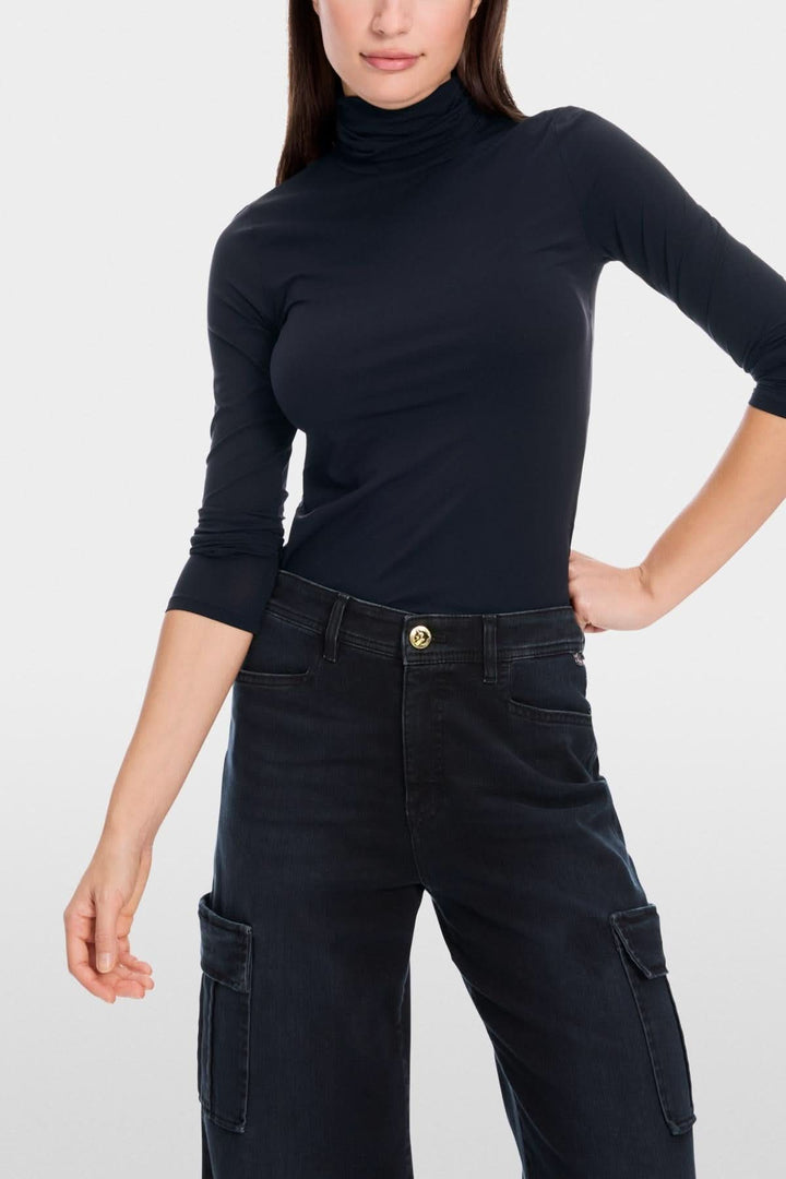 Femme portant un col roulé mince noir avec design épuré, tissu extensible, conseillé sous un veston pour élégance discrète.