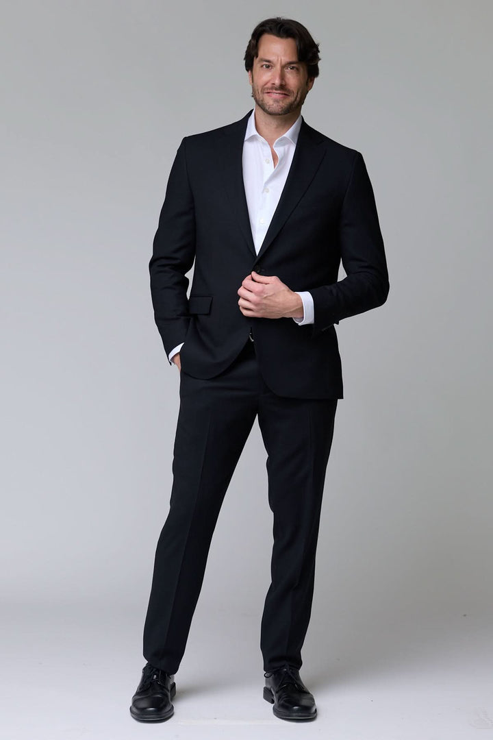 Homme portant un complet classique deux pièces en tissu structuré, soulignant la silhouette avec élégance pour les occasions formelles.