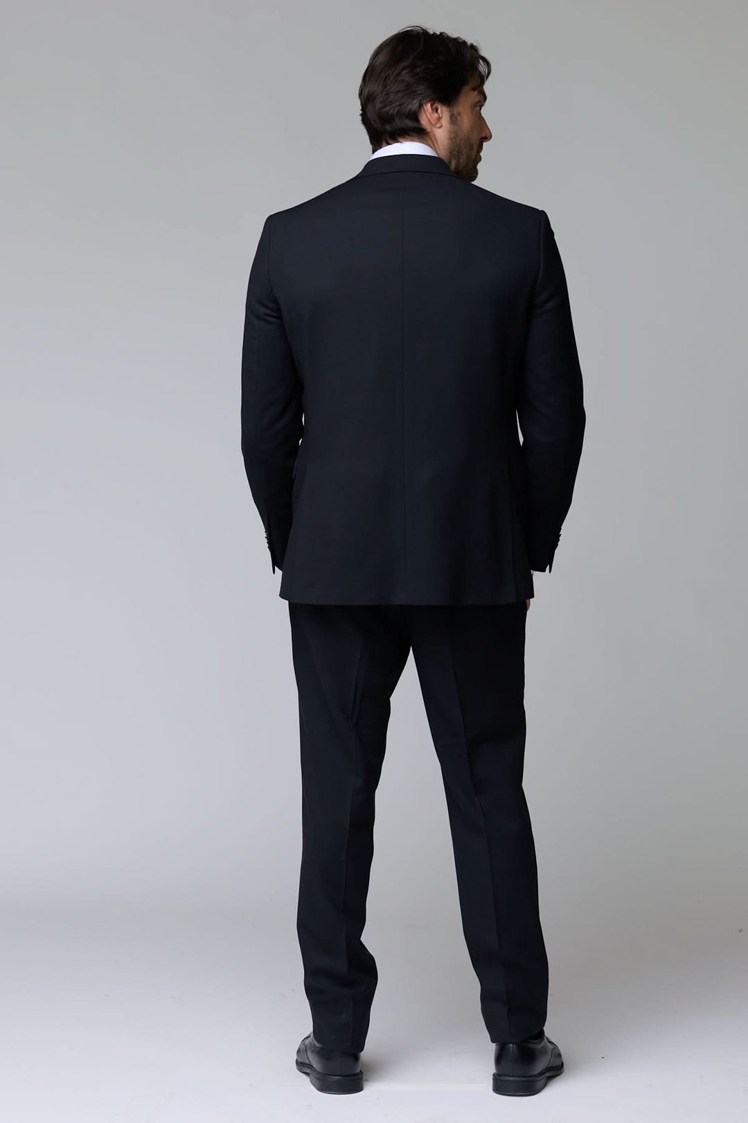 Homme portant un complet classique deux pièces noir élégant vu de dos, parfait pour des occasions formelles et le bureau.
