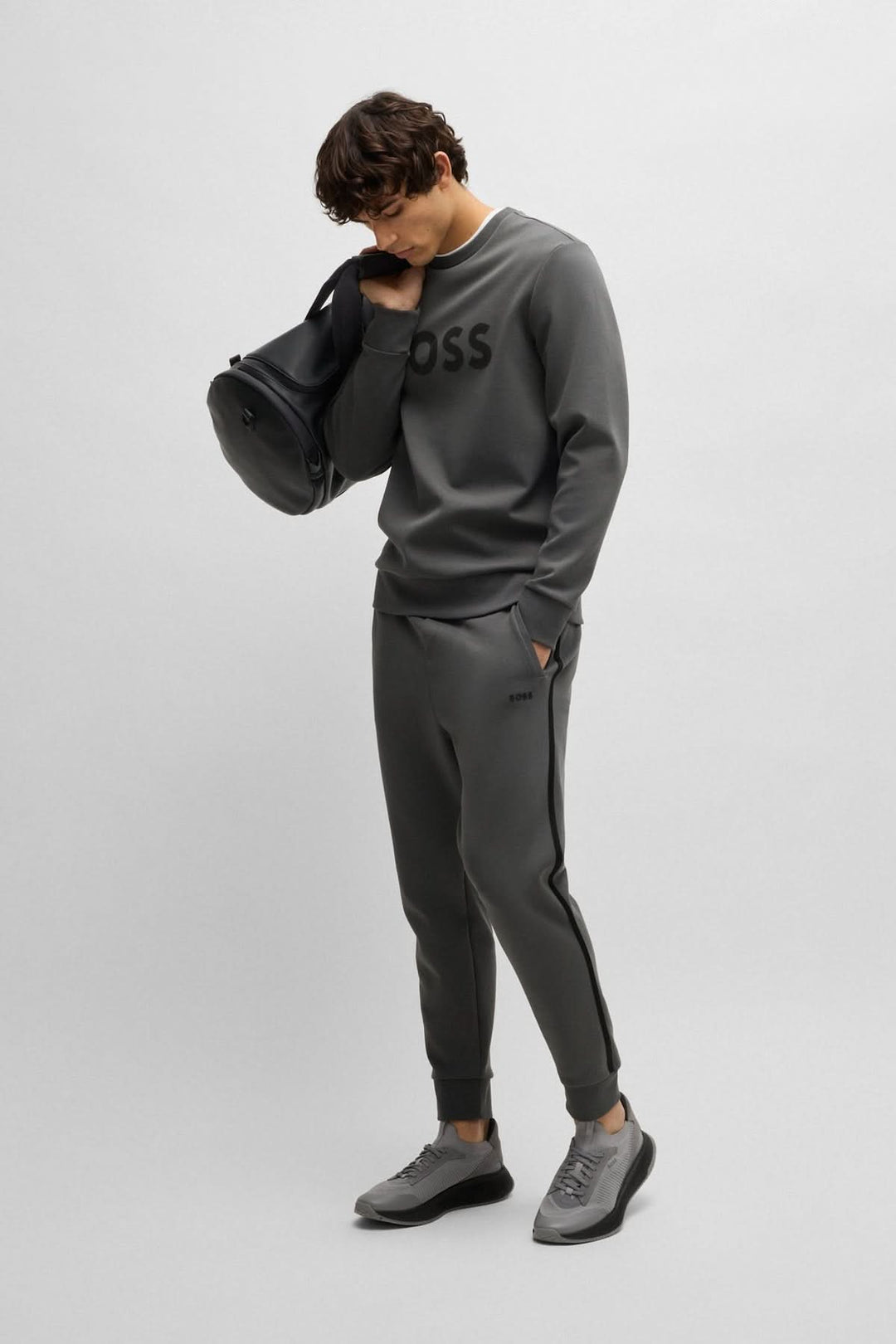 Homme en chandail Coton ouaté Salbo, look moderne avec logo BOSS, pantalon athlétique et sacs noirs.