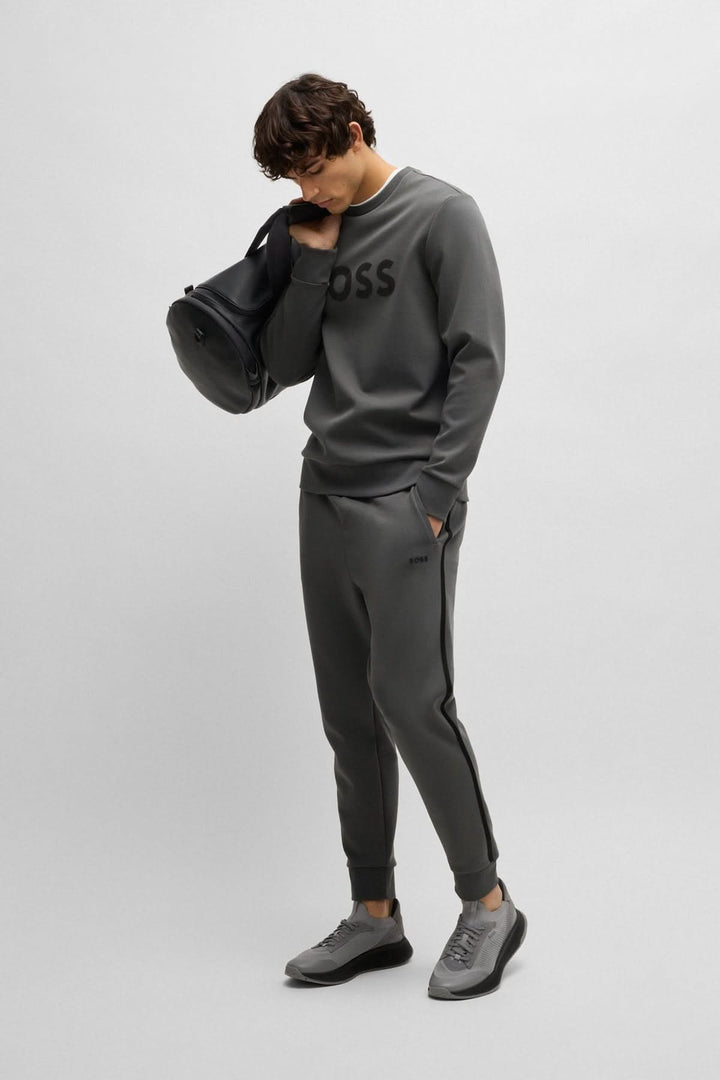 Homme en chandail Coton ouaté Salbo, look moderne avec logo BOSS, pantalon athlétique et sacs noirs.