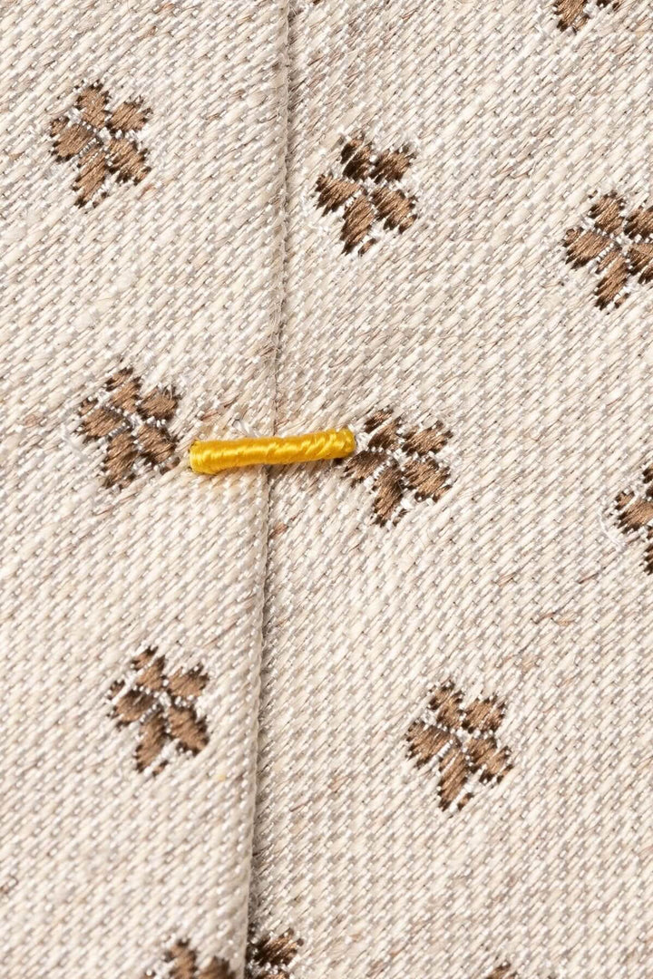 Détail d'une cravate en lin et soie à motif floral beige avec broderie discrète en brun.