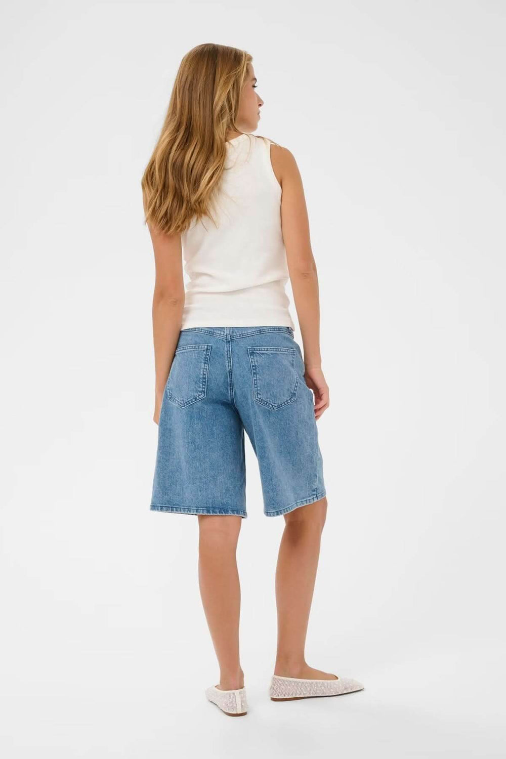 Vue arrière d'une femme portant un débardeur sans manches blanc avec un short en jean.