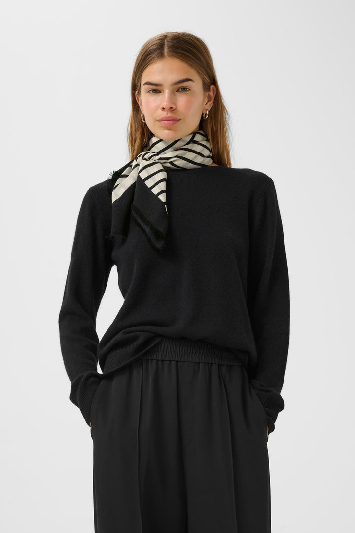 Modèle portant un foulard rayé noir et beige sur un chandail noir, ajoutant une touche élégante à son look.