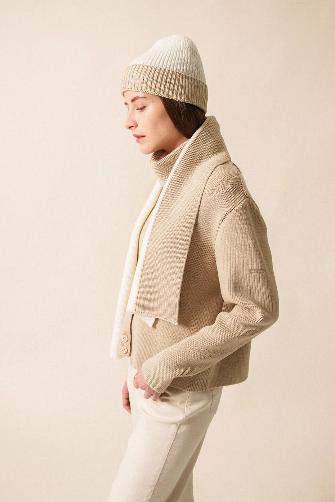 Foulard en maille bicolore porté avec une veste beige et un bonnet, créant un look cosy et élégant.